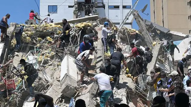 Personas buscan sobrevivientes entre los escombros de un edificio derrumbado.
